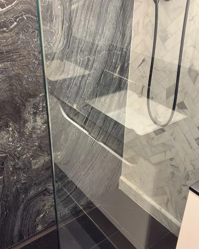 Regadera con pared de mármol oscuro y vidrio sin marcas